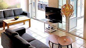 A modern living room with a sofa, coffee table, TV, and a decorative light fixture. - 5 Star Holiday Home in Vaeggerlose (Vaeggerlose)