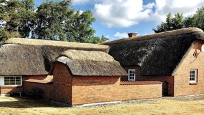 A traditional thatched-roof house with brick walls, a small window, and a door. - 5 Star Holiday Home in Vaeggerlose (Vaeggerlose)