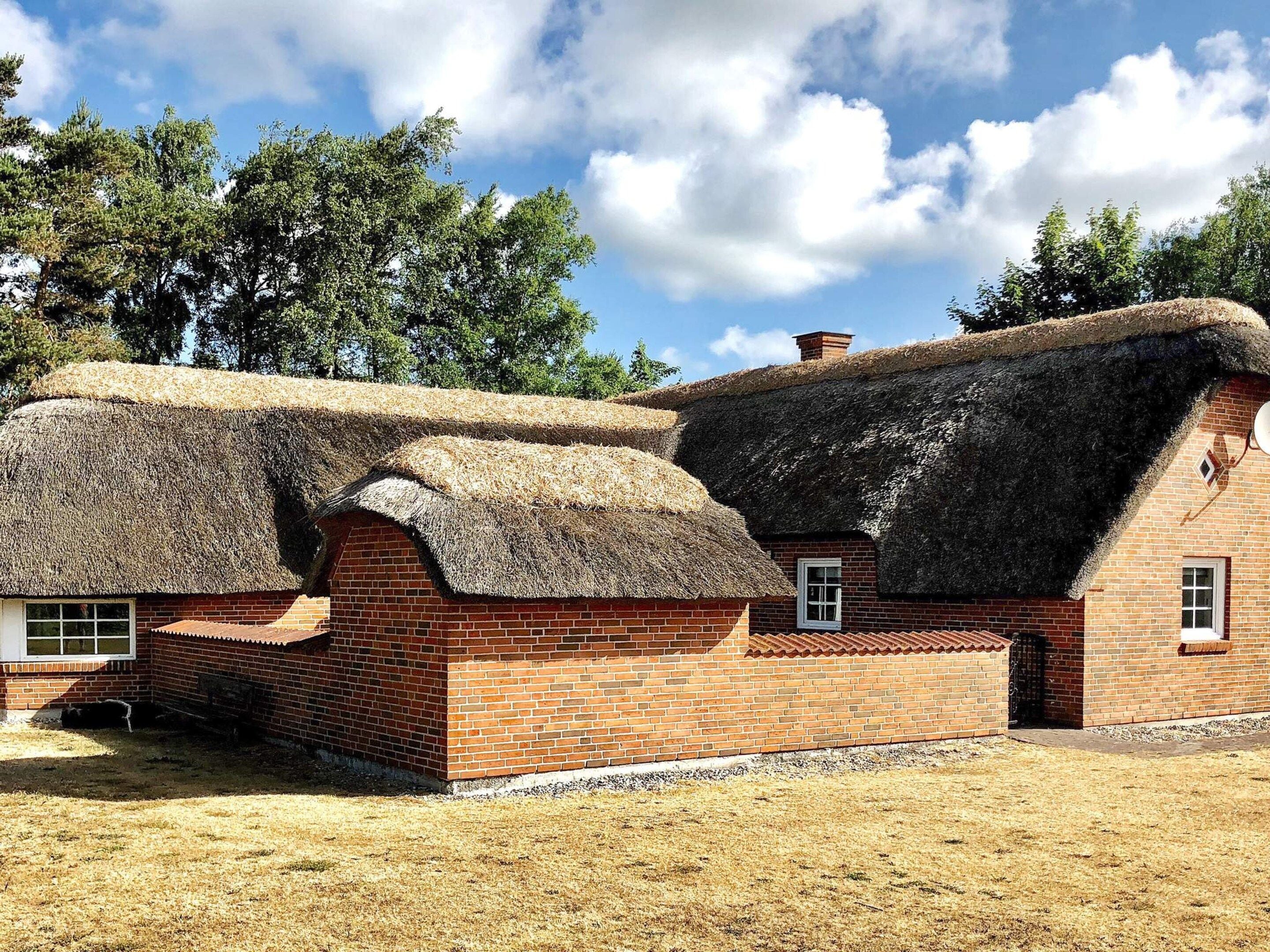 A traditional brick house with a thatched roof and a small attached structure.