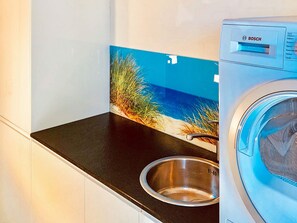 A Bosch washing machine in a kitchen with a black countertop and a stainless steel sink.