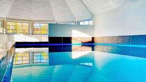 An indoor swimming pool with clear glass walls, a tiled floor, and a high ceiling. - 5 Star Holiday Home in Vaeggerlose (Vaeggerlose)