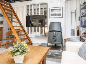 A living room with a wooden ladder, a television, a large grey cabinet, a wicker chair, a white sofa, and a wooden coffee table. - 6 Person Holiday Home in Glesborg (Glesborg)