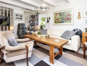 A living room with a checkered floor, a sofa, a chair, a wooden table, a bookshelf, and a painting on the wall. - 6 Person Holiday Home in Glesborg (Glesborg)