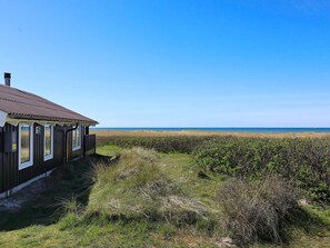 A wooden building with a brown roof, numbered 15, adjacent to a beach with a clear sky.