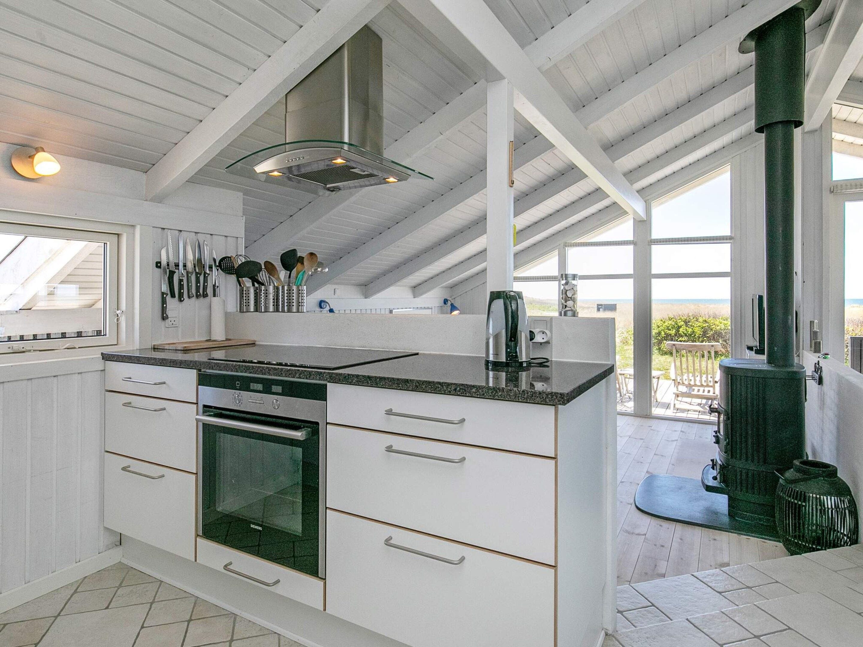 A modern kitchen with a built-in oven, a large window, and a view of the beach.