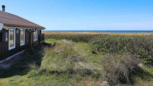 A wooden building with a brown roof and numbered windows, situated near a beach with a clear sky. - 4 Star Holiday Home in Hjorring (Hjørring)