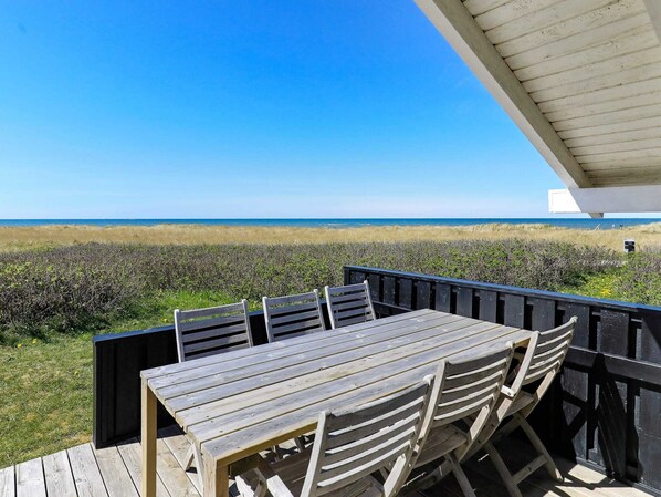 A wooden deck with a table and chairs overlooking a beach.