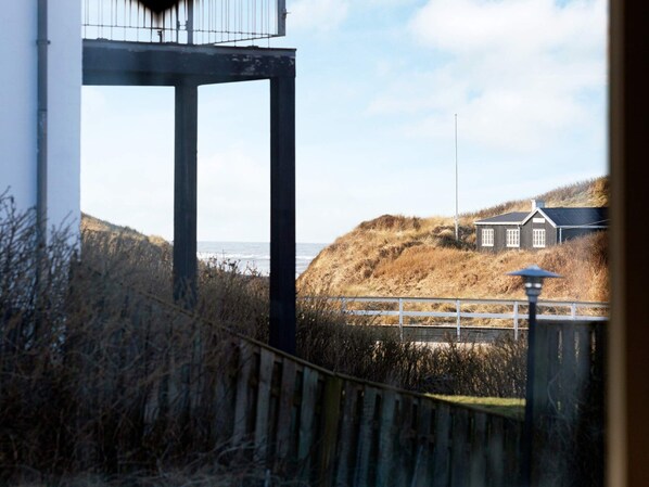 A coastal view with a wooden fence, a white building, and a house on a hill.