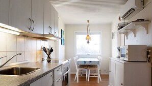 Ett modernt kök med vita skåp, en bänkskiva i granit, en inbyggd ugn och en matplats med ett bord och stolar.