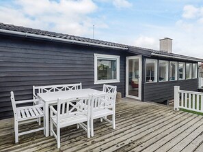 A wooden deck with a white table and chairs, a sliding glass door, and a chimney.