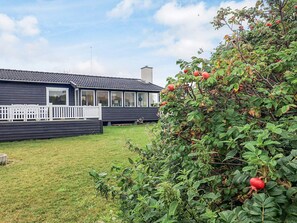 A residential property with a dark-colored house, a white fence, and a garden with green foliage and red berries.