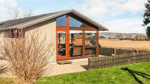A modern house with a large glass door and windows, a wooden deck, and a view of a lake. - 4 Star Holiday Home in Juelsminde (Juelsminde)