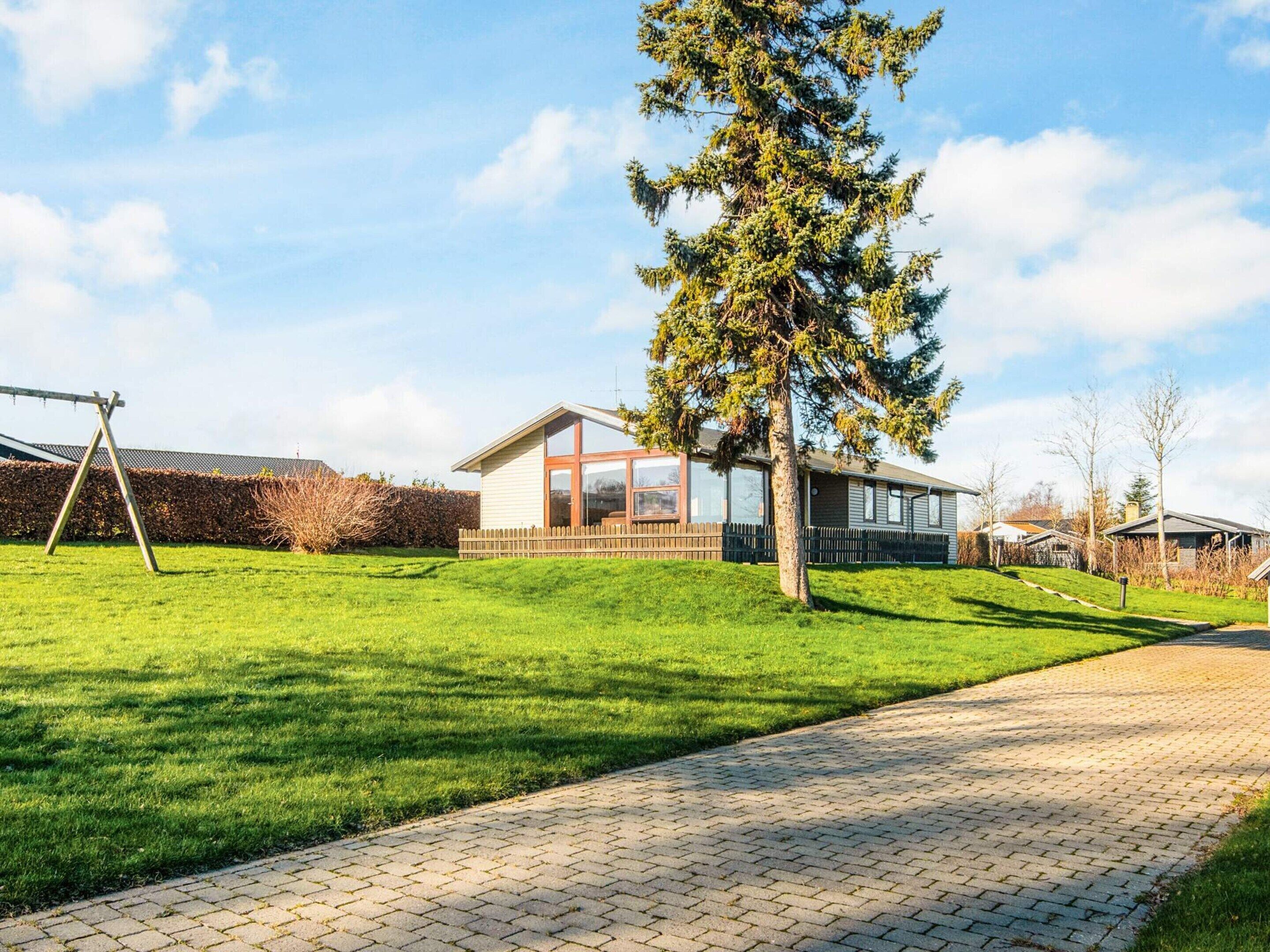 A residential area with a modern house featuring large windows, a paved driveway, and a well-maintained lawn.