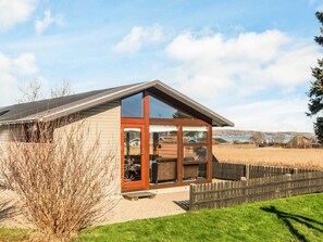 A modern building with a glass entrance, a wooden deck, and a view of a lake.