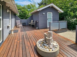 A wooden deck with a stone centerpiece, a small cabin with a window, and outdoor seating.