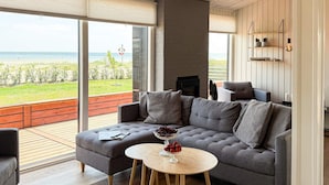 A modern living room with a grey sectional sofa, a round wooden coffee table, and a view of the beach through large windows. - Peaceful Holiday Home in Fjerritslev near Beaches (Sjølund)