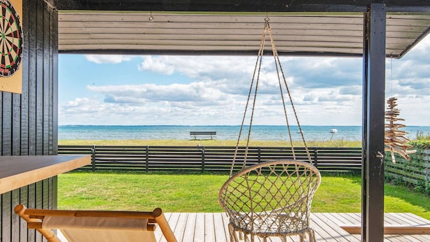 A wooden deck with a hammock chair and a table, overlooking a beach with a bench and a fence. - Peaceful Holiday Home in Fjerritslev near Beaches (Sjølund)