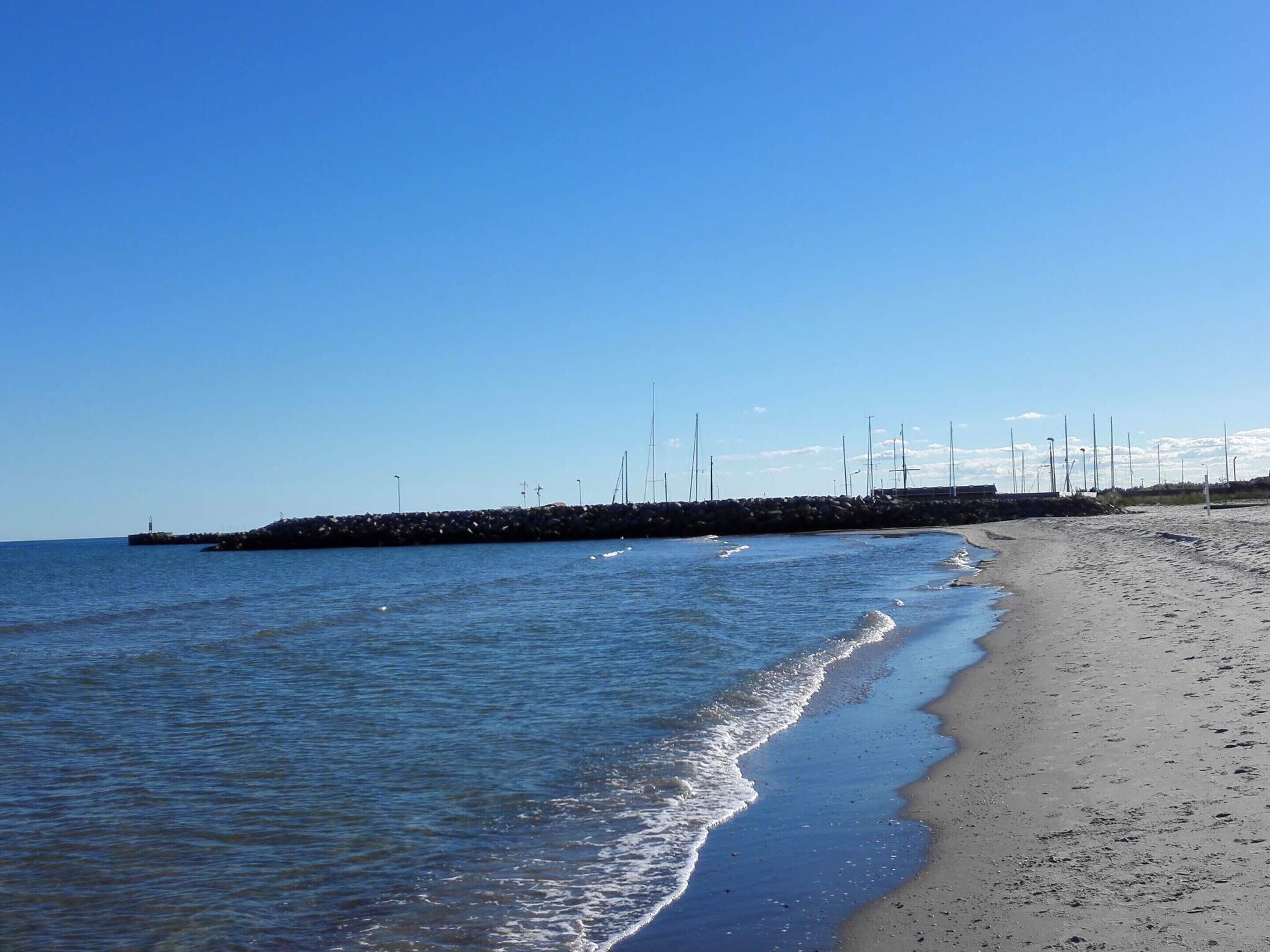 A beach with a rocky breakwater, calm water, and a clear sky.