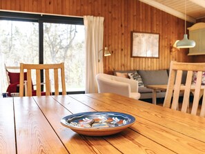 A wooden dining table with a decorative bowl in the center, a wooden chair, a sofa, and a pendant light in a room with wooden walls and a window. - Pretty Holiday Home in Ålbæk near Sea (Aalbaek)