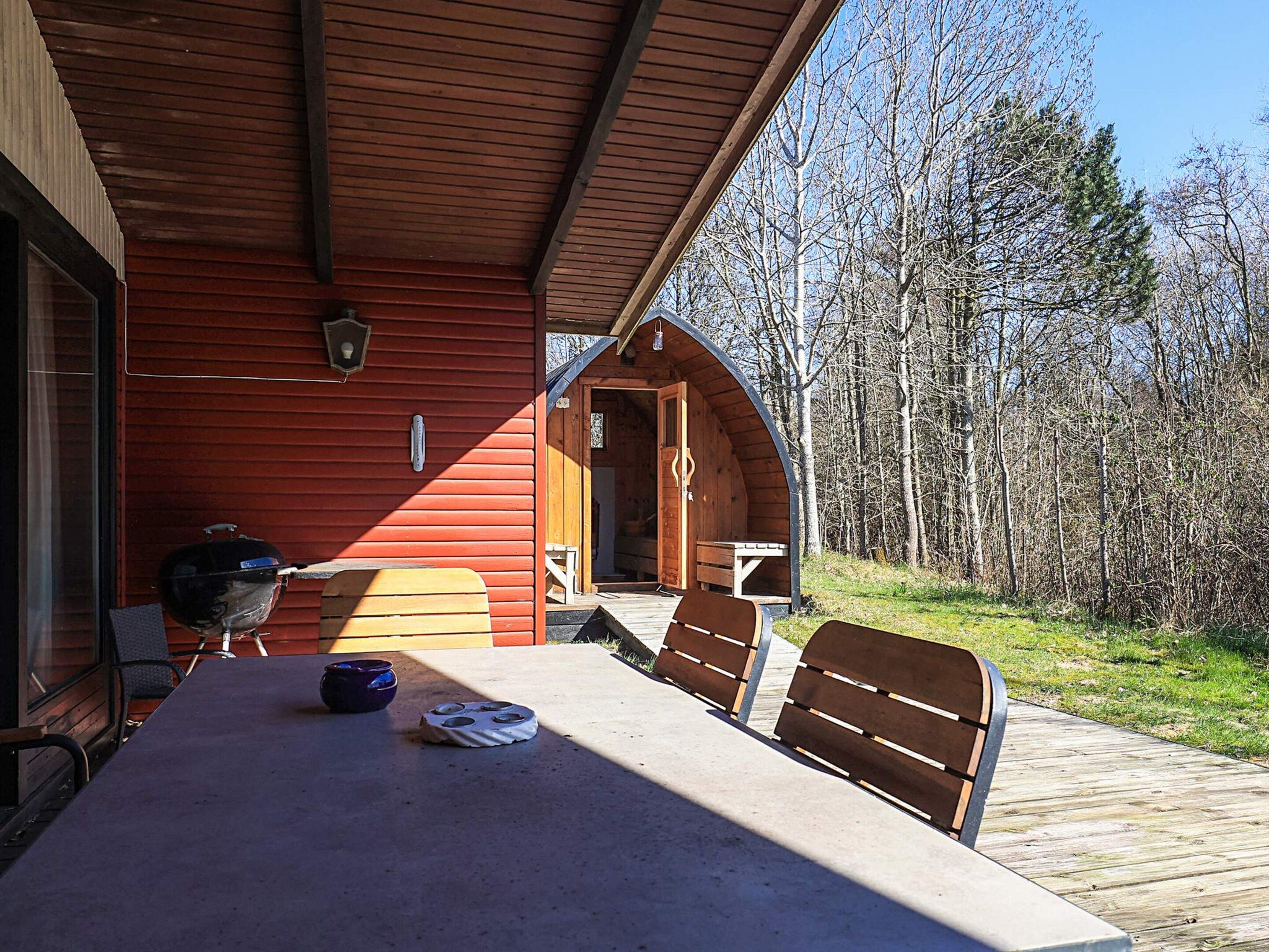 A wooden cabin with a covered patio, outdoor seating, and a grill.