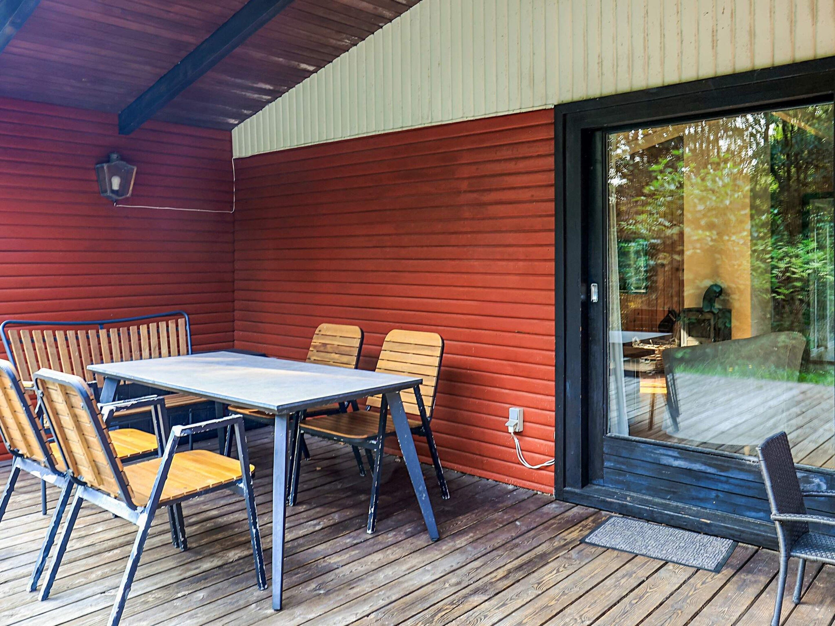 Een overdekt terras met een tafel en stoelen, een houten terras en een schuifdeur naar een terras met tuinmeubels.