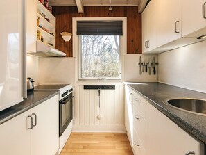 A compact kitchen with white cabinetry, a built-in oven, a window with a view of trees, and a countertop with a sink. - Pretty Holiday Home in Ålbæk near Sea (Aalbaek)