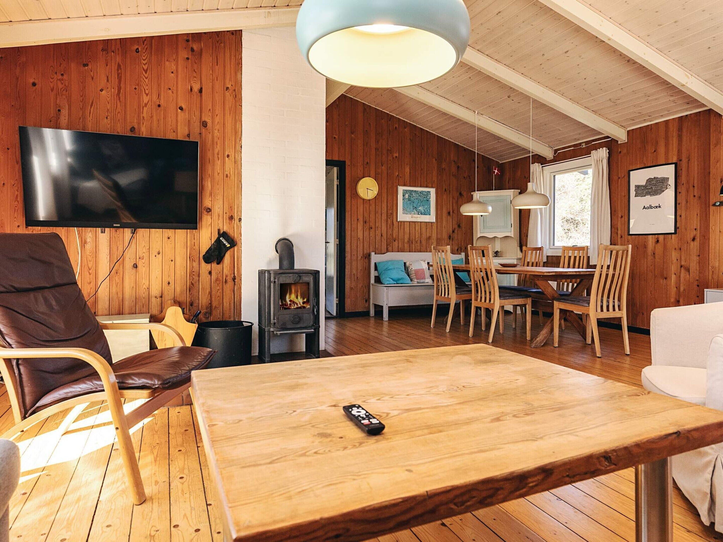 Una habitación acogedora con detalles de madera, un televisor en la pared, chimenea, comedor con sillas y mesa, y un sofá.