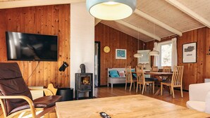 A cozy room with a wooden interior, a TV mounted on the wall, a fireplace, a dining area with chairs and a table, and a sofa. - Pretty Holiday Home in Ålbæk near Sea (Aalbaek)