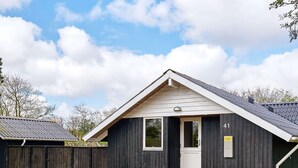 A small, dark wooden building with a white door and windows, a gravel driveway, and a wooden deck. - 6 Person Holiday Home in Hemmet (Hemmet)