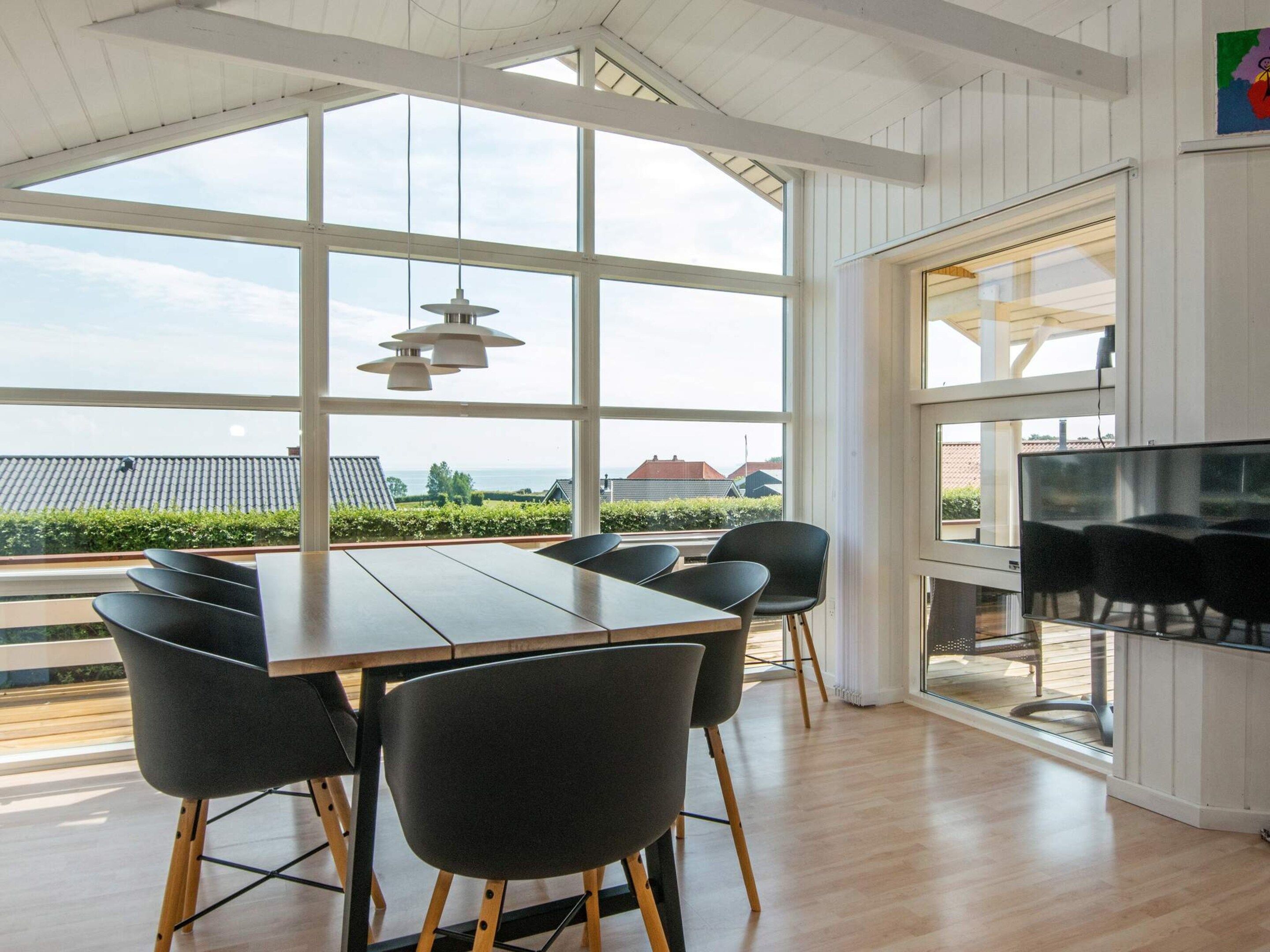 A modern dining area with a large table and chairs, large windows, and a television.