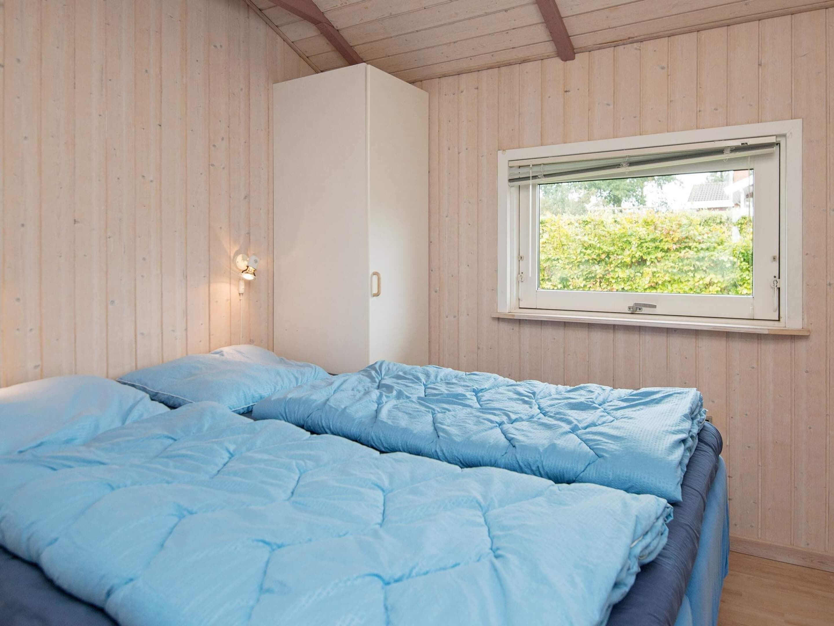 A bedroom with a bed, a window, and a wall-mounted light fixture.