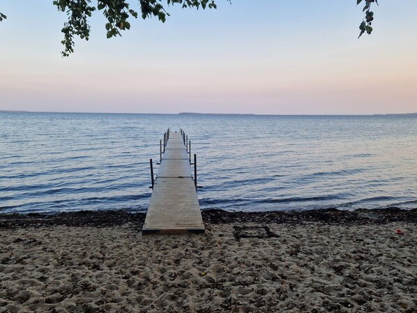 A wooden pier extending into calm water, surrounded by sandy beach.