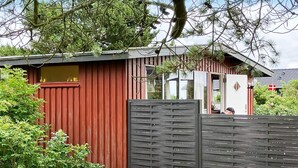 A red wooden building with a dark wooden gate, surrounded by greenery. - 5 Person Holiday Home in Lemvig (Lemvig)