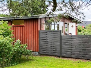 A red wooden building with a dark wooden fence, surrounded by greenery.