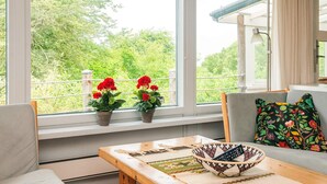A room with a wooden table, a sofa, and a window with potted plants. - Quaint Holiday Home near Glesborg with Roofed Terrace (Glesborg)
