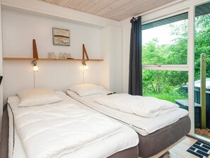 A bedroom with two beds, a wooden shelf with decorative items, a wall-mounted light, and a window with a view of greenery. - Quaint Holiday Home near Glesborg with Roofed Terrace (Glesborg)