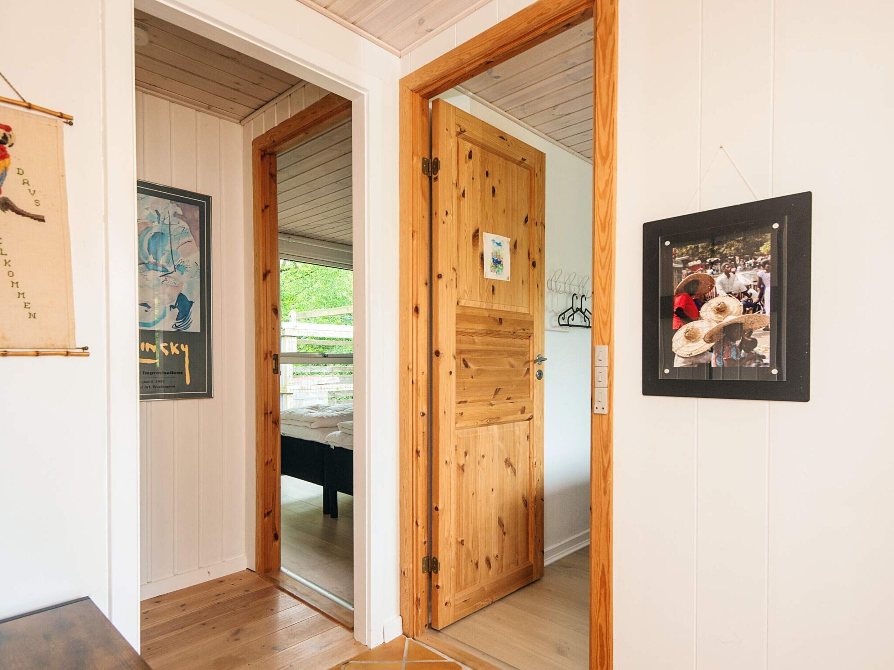 A hallway with wooden doors, a bed, and framed artwork on the walls.