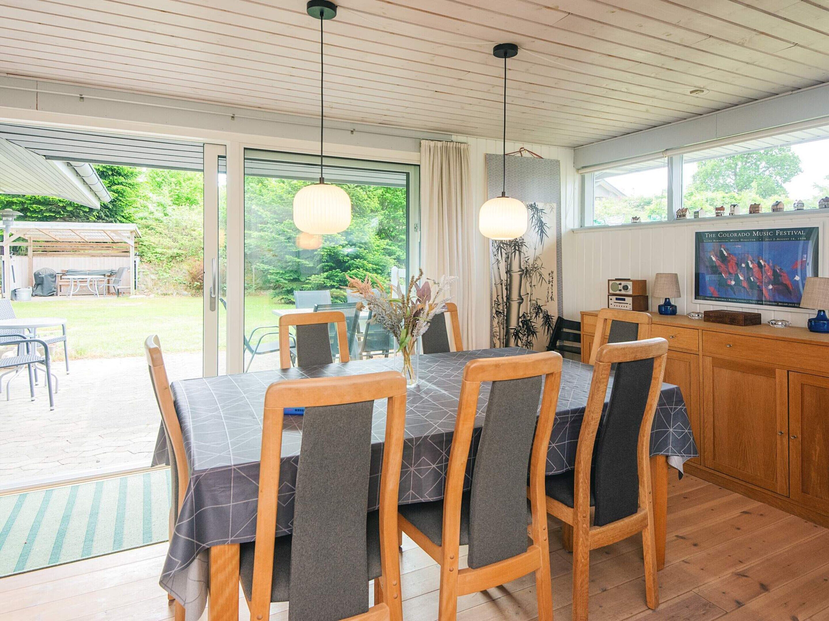 Een eetruimte met een tafel voor vier personen, houten stoelen, een vaas met bloemen en een televisie waarop 'The Colorado Music Festival' te zien is.
