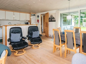 A modern kitchen with white cabinets, a dining area with wooden chairs and a table, and a large window with a view of greenery. - Quaint Holiday Home near Glesborg with Roofed Terrace (Glesborg)