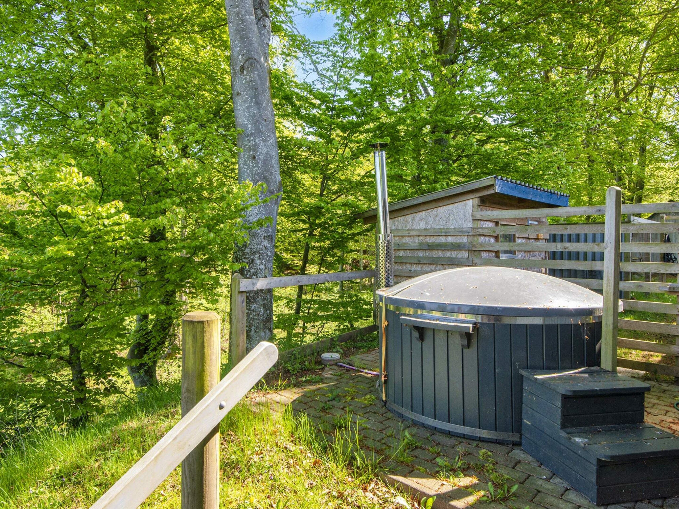 Un jacuzzi en un área boscosa con cerca de madera y un cobertizo pequeño.
