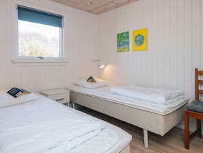 Ein Zimmer mit zwei Betten, einem kleinen Nachttisch, einem Stuhl und einem Fenster mit Jalousien.