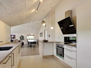A modern kitchen with white cabinetry, a dining area with a table and chairs, and a TV mounted on the wall.
