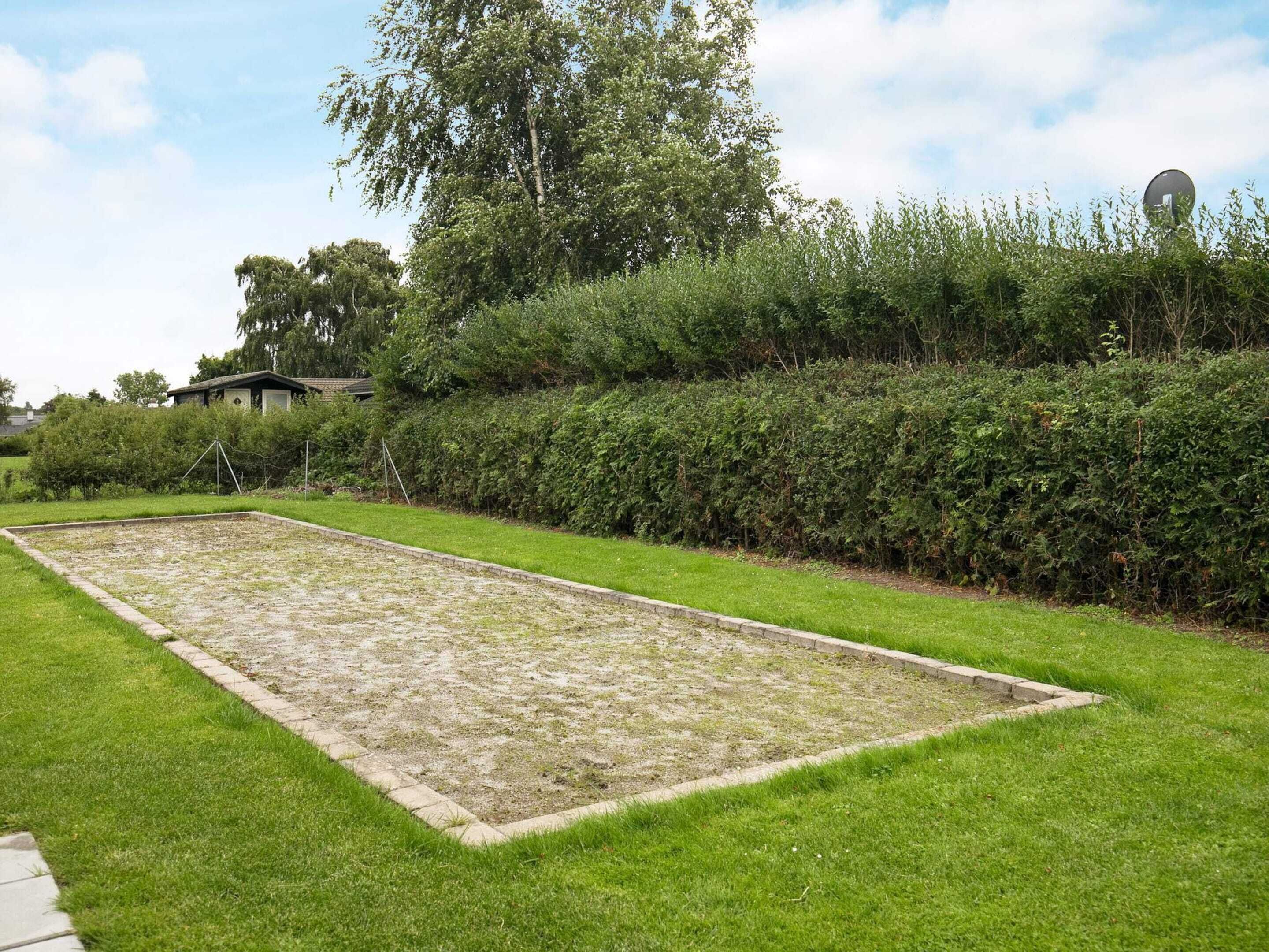 A rectangular outdoor area with a grassy border, a hedge, and a building in the background.