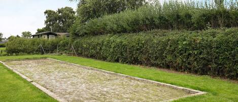 A rectangular outdoor area with a grassy border, a hedge, and a building in the background.