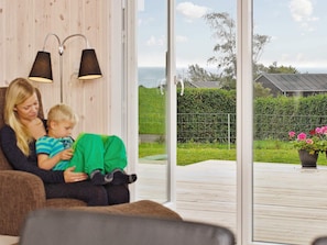 A room with a large window, two wall-mounted lamps, and a view of a garden with a fence and flowers.