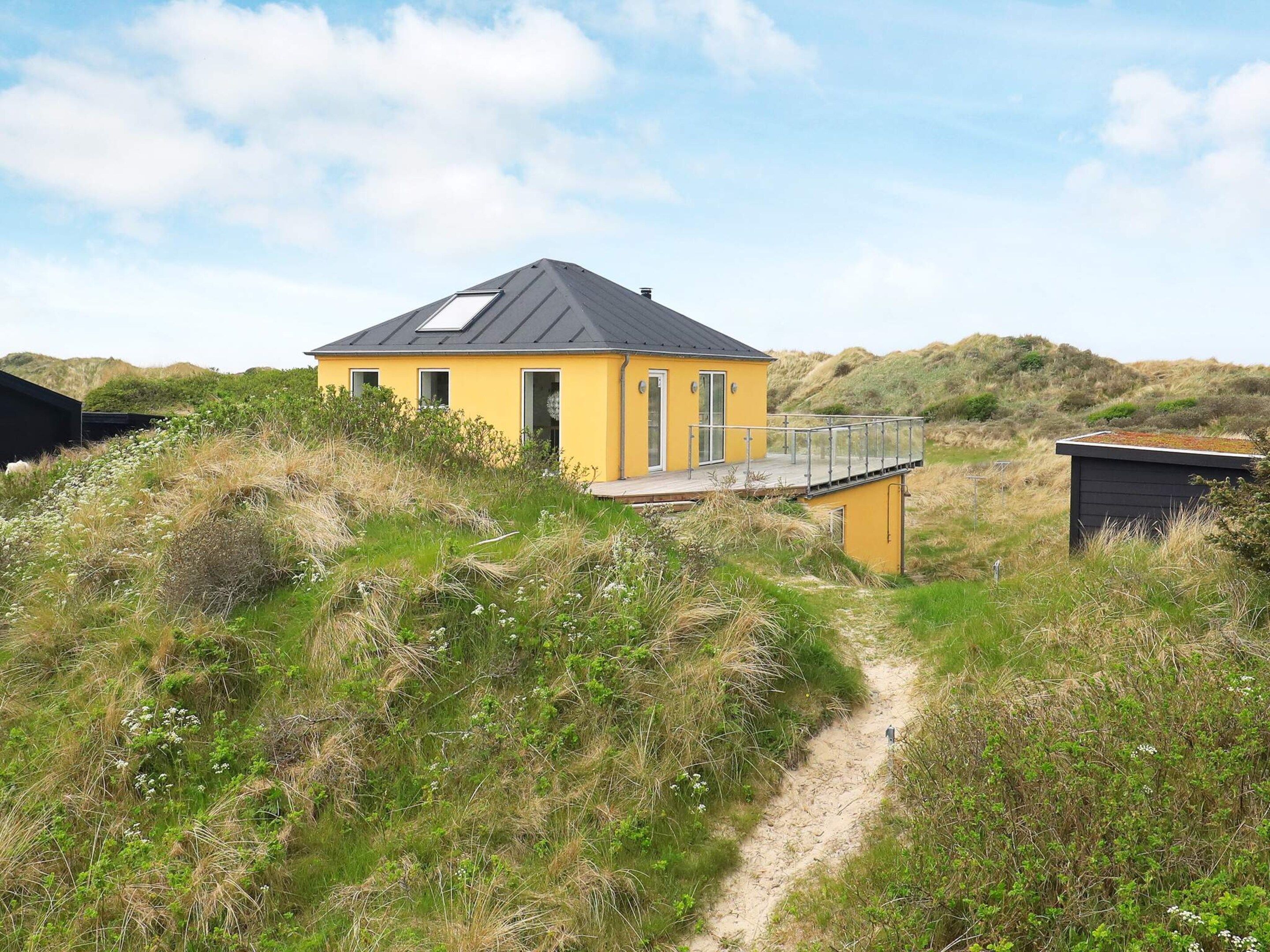 A yellow building with a black roof, surrounded by natural vegetation and a clear sky.