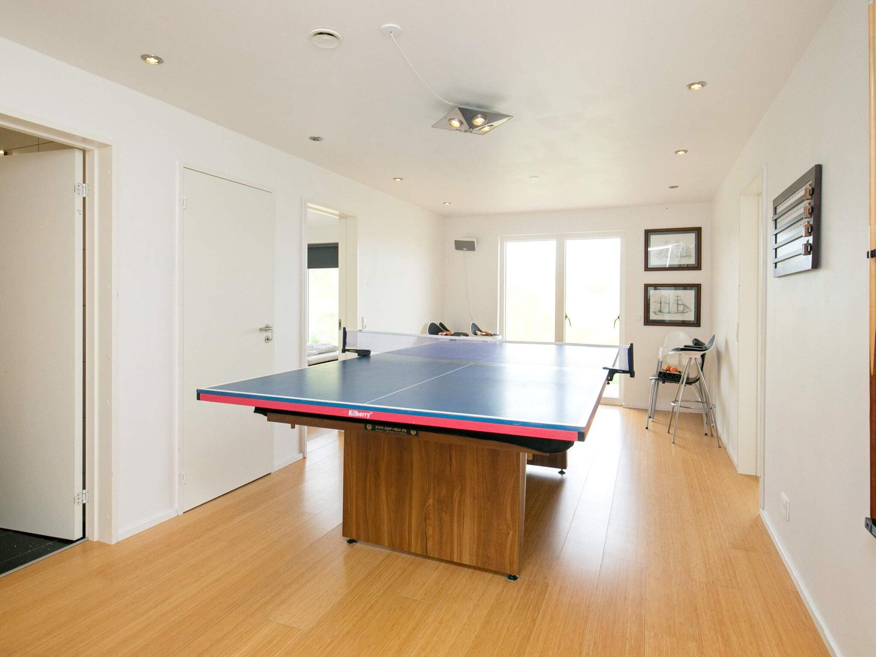Habitació amb taula de ping-pong, sòl de fusta i una porta que dóna a una altra estança.