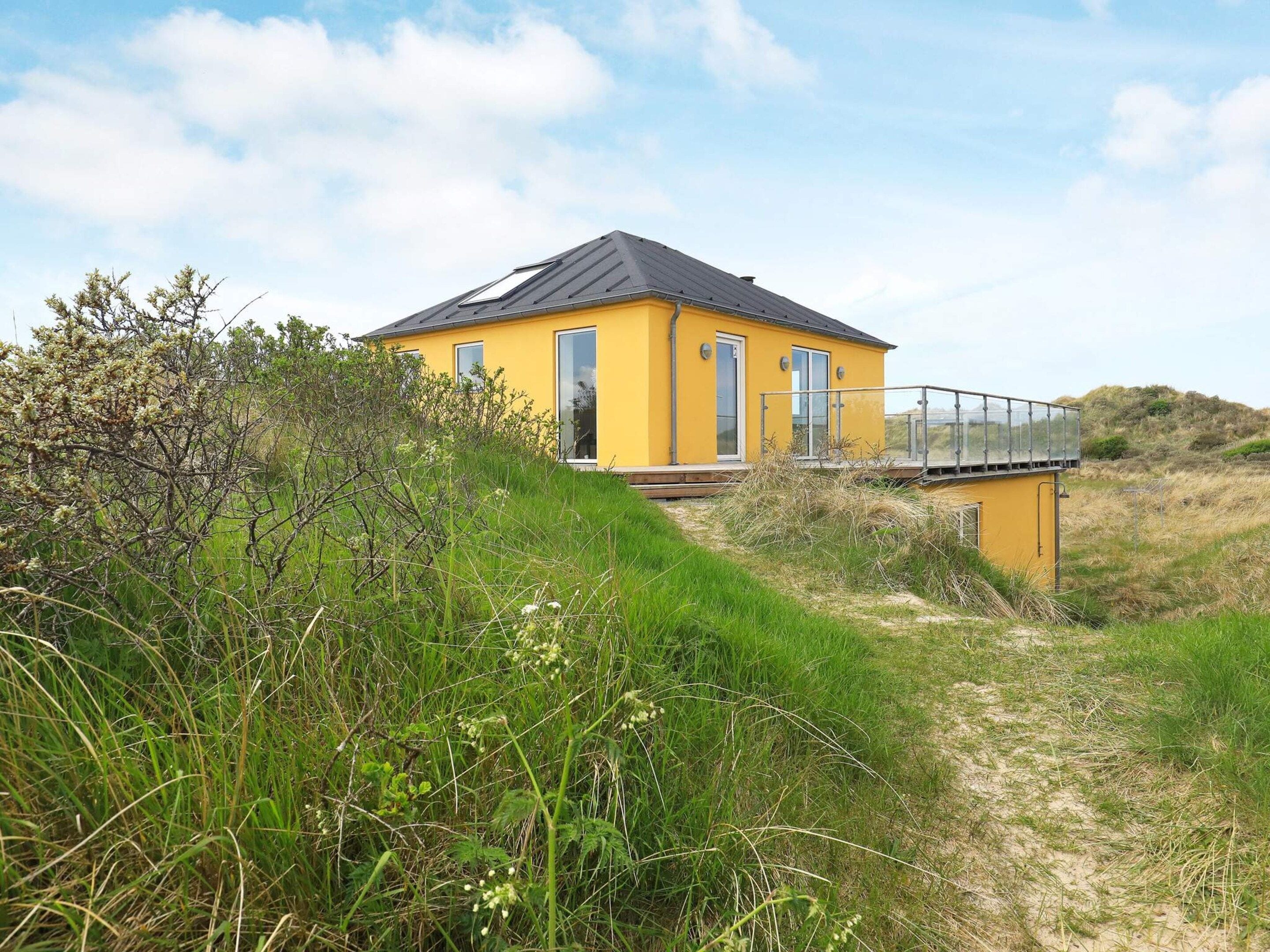 A yellow building with a balcony, surrounded by natural vegetation.
