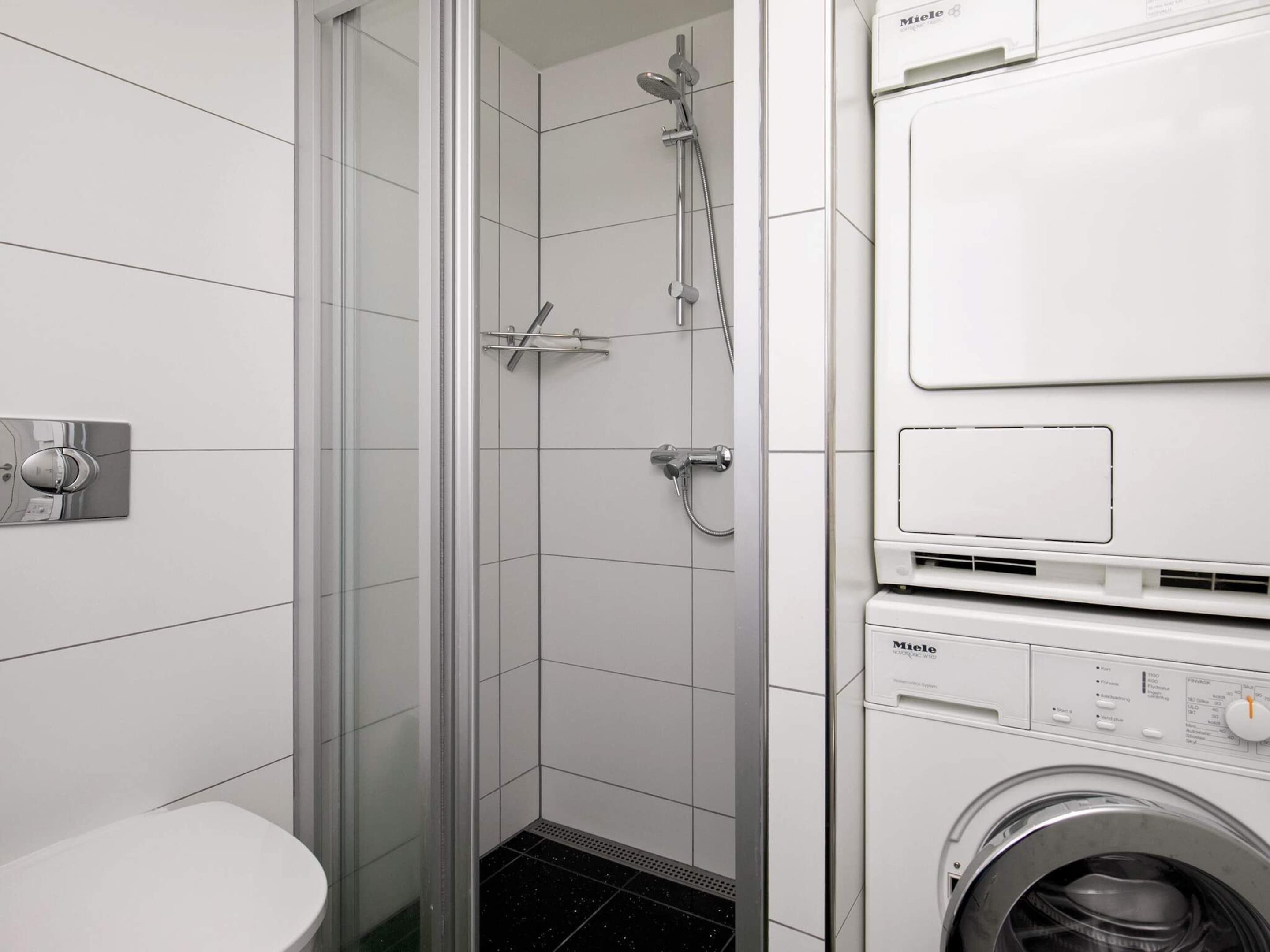 Een moderne badkamer met een douchecabine van glas, een toilet en een wasmachine met voorlaadklep.