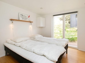 A bedroom with a bed, a wall-mounted shelf with a picture, a cabinet, and a sliding glass door leading to an outdoor area.